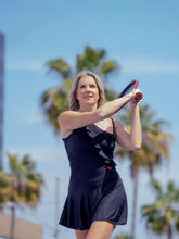 Load image into Gallery viewer, The Charmaine Court To Cocktails Tennis Dress in Black. Flirty and alluring. That's the Charmaine tennis dress. Wear this sexy dress from the court to cocktails. The off the shoulder neck, asymmetrical lines, and side slit make this our most sexy dress. It is a fitted cut, but lined to give support, and is sewn with our silky soft stretchy fabric. This dress is short, it sits high on the thigh. This dress comes with its own one-sided matching soft bra to wear underneath.